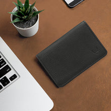 Load image into Gallery viewer, Black leather bifold wallet on brown desk beside laptop, smartphone and small potted plant flat lay.