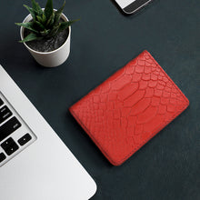 Load image into Gallery viewer, Red textured leather card holder on a dark desk beside a laptop, phone, and a small potted plant.