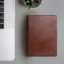 Load image into Gallery viewer, A dark tan leather bifold wallet next to a silver laptop and a small succulent plant from Hidesign.