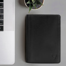 Load image into Gallery viewer, Black leather bi-fold wallet for men, placed beside a laptop and a plant for a modern, minimal look.