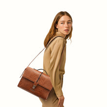 Load image into Gallery viewer, Woman in beige outfit carrying a textured tan leather shoulder bag with flap lock from Hidesign.